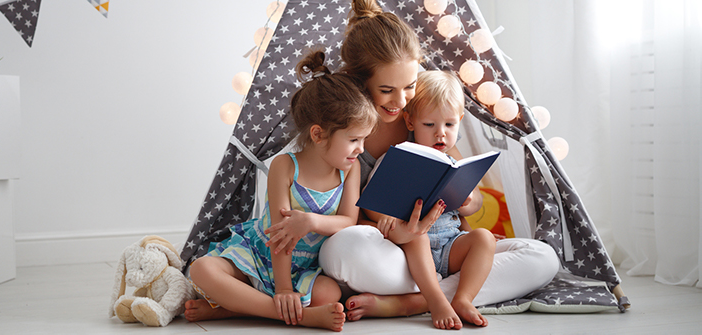 Mamă tânără, cu doi copii în brate, în timp ce le citește dintr-o carte